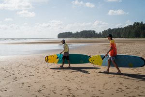 A surfing student walks into the sea with their teacher in Khao Lak, the only place known for surfing in Thailand. To grow tourism in underserved areas of Thailand, the country's marketing agency, the Tourism Authority of Thailand (TAT), has launched campaigns to promote international tourism to the south as a part of its "Amazing New Chapters" campaign. This specific part of the campaign targets Phuket, Phangan, and Khao Lak, an area known to be the only place to go surfing in Thailand.