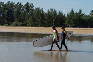 A surfing student walks into the sea with her teacher in Khao Lak, the only place known for surfing in Thailand. To grow tourism in underserved areas of Thailand, the country's marketing agency, the Tourism Authority of Thailand (TAT), has launched campaigns to promote international tourism to the south as a part of its "Amazing New Chapters" campaign. This specific part of the campaign targets Phuket, Phangan, and Khao Lak, an area known to be the only place to go surfing in Thailand.