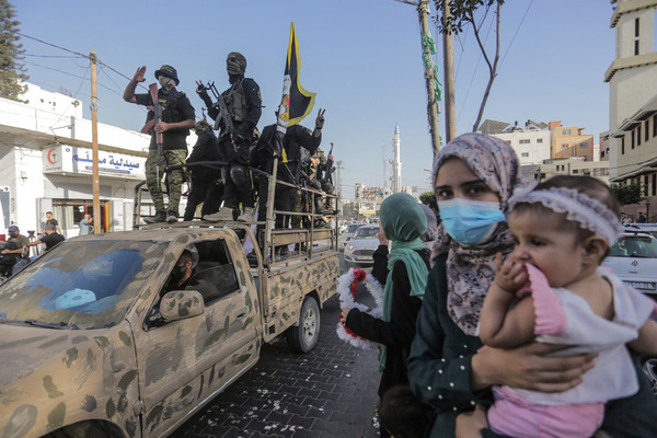 A Palestinian woman holds her child while looking at the armed fighters from Saraya al-Quds, the military wing of Islamic Jihad, as they take part during an anti-Israel military parade on the 35th anniversary of the launch of the Islamic Jihad Movement in Gaza City.