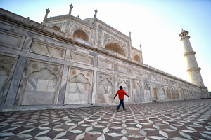 A man seen walking beside the wall of the Taj Mahal. The Taj Mahal is a mausoleum located in the right bank of the river Yamuna - Agra, India, built by Mughal Emperor Shah Jahan in memory of his favorite wife, Mumtaz. The Taj Mahal is considered the finest example of Mughal architecture, a style that combines elements from Persian, Oman, Indian, and Islamic architectural styles. The Taj Mahal is in the list of modern Seven Wonders of the World and It has also been a protected UNESCO World Heritage Site since 1983.