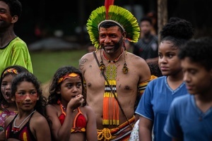 An indigenous man wearing traditional outfit and ornaments surrounded by a group of people during the celebrations of the Indigenous People’s Day, at the Aldeia Katurãma.