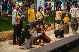 Young women are seen taking pictures while their friend is praying in front of her Krathong during the Magical Loy Krathong Festival at Jodd Fairs Dan Neramit in Bangkok. Loy Krathong, Thailand's Festival of Lights, is celebrated annually across Thailand and nearby regions. During this festival, people float decorated baskets made of banana leaves, incense sticks, and candles on rivers, canals, or ponds. They make wishes as they release these baskets.