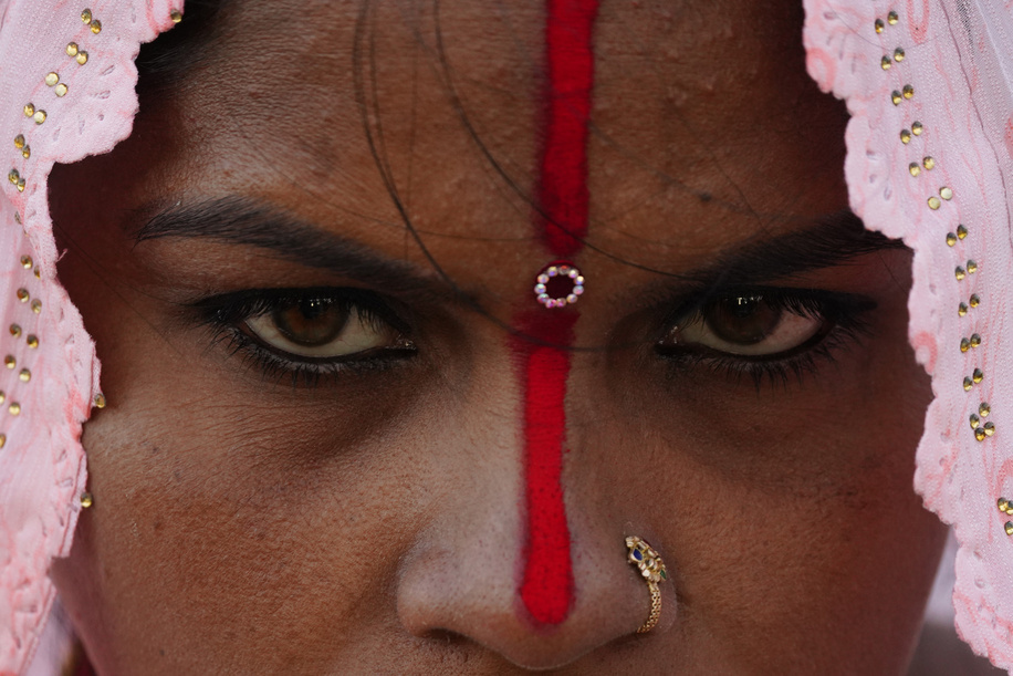 A Nepalese Hindu woman looks on with her face painted red stripe with a jewellery ring in her nose while offering prayers to the setting sun on the banks of the Bagmati river during the Chhath festival in Kathmandu. On the day of Chhath, an ancient festival observed by Hindus, devotees gather by the holy river to offer prayers by fasting, bathing, and standing in the water for continuous periods to offer prayers to the Sun God, thanking and paying respects to seek blessings for sustaining life on earth.