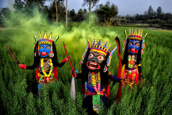 Masked dancers of the Gomira dance troupe perform in a big mustard field in a village near Raiganj. Gomira is a masked dance form. The word ‘Gomira’ is derived from the colloquial form of the word ‘Gram-Chandi’ or the female deity who is the protective force of the village. The exact origin of the dance form is not traceable and the knowledge has been lost over time. Gomira dance is a rural dance form mainly practiced in the Dinajpur district of West Bengal. The Gomira dances are organized to appease the deity to usher in the 'good forces' and drive out the 'evil forces'. It is usually organised during mid-February to mid-July. There are no fixed dates but each village has its own Gomira dance troupe and organizes at least one dance performance during this period. The use of wooden masks is characteristic of the dance festivals of the Gomira.