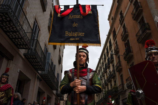 A man dressed as a Roman carries a banner that says "Armats de Balaguer" during the procession of the Good Death. Procession of the Good Death was organized by the Congregation of the Christ of the Good Death in Barcelona.
