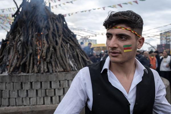 A young man who has his face painted waits in front of the Newroz fire during a rally. Hundreds of thousands of people attend Diyarbakir Newroz to celebrate Newroz, which symbolizes the arrival of spring and the new year. Since it is forbidden to bring yellow, green and red flags to the Newroz area, people painted their faces in yellow, red and green colors.