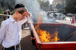 A Jewish boy stands next to the fire looking at a burning leaven during the Biur Chametz. During the Biur Chametz, religious Jews fulfill their obligation to inspect their homes for any leaven and eliminate it before the night of Passover. In ultra-Orthodox cities in Israel, fires are set up in major locations in the city for this purpose, where people bring their bread leftovers to burn the leaven. During the seven days of Passover, they are prohibited from eating or possessing any leaven, symbolizing the dough the Israelites did not have time to allow to rise before the Exodus from Egypt. Biur Chametz, also known as 'the burning of the leavened goods,' is a Jewish ceremonial ritual involving the burning of leavened foods (chamets) to mark the start of Passover.
