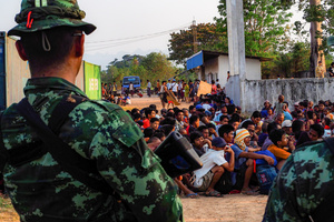 A Thai soldier stands in front of the Myawaddy war refugees. On April 12, Karen KNLA and PDF forces raided the army's 275th military garrison in Myawady town, prompting more than 100 soldiers to attempt to flee to Thailand across Friendship Bridge No. 2. The KNLA/PDF joint forces subsequently attacked these soldiers on the night of April 19th. According to residents, the military council's air response included no fewer than 40 bombs being dropped. As a result of the fighting, approximately 2,000 people fled to Mae Sot, Thailand, across the Moei (Thaung Yin) River.