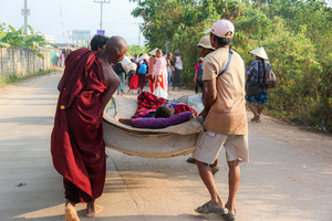 Men and a novice monk are seen carrying a sick elderly man as they flee from the Myawaddy War to Mae Sot. On April 12, Karen KNLA and PDF forces raided the army's 275th military garrison in Myawady town, prompting more than 100 soldiers to attempt to flee to Thailand across Friendship Bridge No. 2. The KNLA/PDF joint forces subsequently attacked these soldiers on the night of April 19th. According to residents, the military council's air response included no fewer than 40 bombs being dropped. As a result of the fighting, approximately 2,000 people fled to Mae Sot, Thailand, across the Moei (Thaung Yin) River.