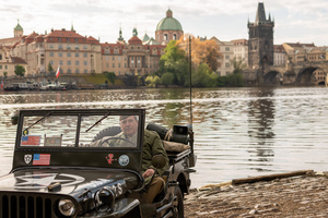 A history enthusiast dressed in World War II US Army uniform seen driving historical army jeep in front of famous Charles Bridge before the Convoy of Liberty event in Prague. The Convoy of Liberty commemorates the liberation of the western part of the Czech Republic from Nazi occupation by the US Army, as well as the 79th anniversary of the end of World War II in 1945. Throughout the convoy, individual military history clubs and army forces re-enactors join the routes of Allied armies.