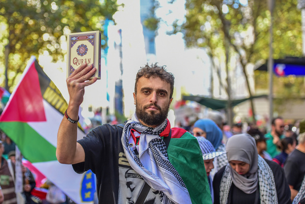 A protester draped with the Palestinian flag holds a Quran during the demonstration. Pro-Palestinian protesters staged a demonstration march through the streets of Melbourne central business district towards the Parliament of Victoria in Melbourne.