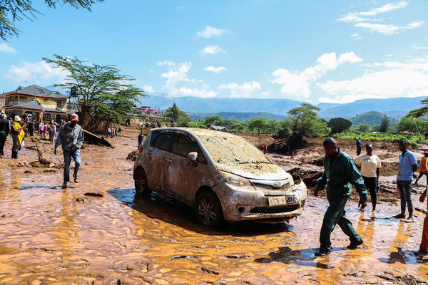 People walk past a car damaged by floods. More than 50 people have been reported dead and hundreds more missing after a heavy rainfall caused floods.