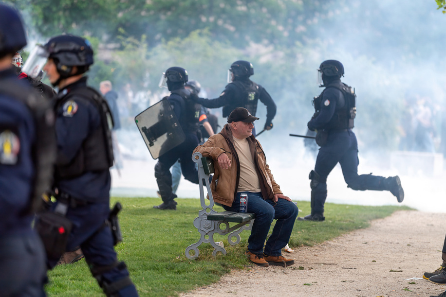 A man sits on a park bench with a beer as riot police charge into the park at Nation during the annual International Workers Day march in Paris France on the 1st of May, May day. Paris streets echo with fireworks and stunt grenades during May Day protests as workers assert their rights amid a sea of banners and chants. Amidst the fervor, clashes break out between demonstrators and riot police, tear gas filling the air as tensions escalate. The event underscores the ongoing struggle for labor rights and social justice, as activists unite in a collective call for change on the streets of the French capital.