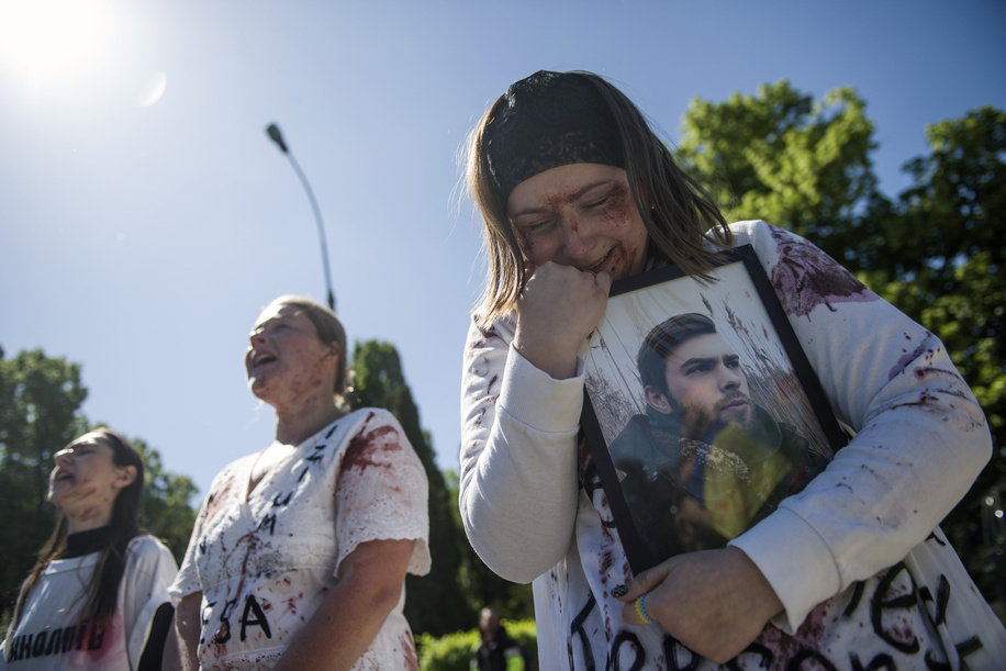 A Ukrainian woman covered with fake blood cries over a portrait of her family member, while Russian ambassador puts flowers at the monument at the cemetery to Red Army soldiers. On Russia's 