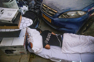 An Israeli youth sleeps along the street near his belongings evacuated from damaged apartments next to a residential building in Beíer Sheva destroyed by an Iranian ballistic missile, in which four Israelis were killed .