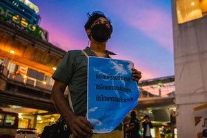 A protester holds a placard reading “People’s Amnesty” at sunset during a vigil. People gathered outside Bangkok Art and Culture Centre for a candlelight vigil titled “Light Up Hope for the People’s Amnesty.” Organized ahead of a parliamentary debate on the 16 July 2025, the event featured personal testimonies, portraits of 50 political detainees, and a red rose display reading “Amnesty 112.” Participants called for the passage of a comprehensive amnesty bill covering cases under Section 112 of the Thai Criminal Code.