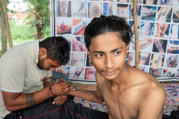 A devotee seen getting a tattoo on his hand done at a tattoo art shop during the holy month of Sawan (Shravan), a grand Kanwar Mela or religious fair is held at Chhota Haridwar. During this time, the fair is crowded with Kanwar devotees ( People who take part in the Kanwar Yatra to worship Lord Shiva by carrying holy water and offering it at Shiva temples) , most of whom wish to preserve the memory of this religious Kanwar Yatra by making it memorable through tattoos.