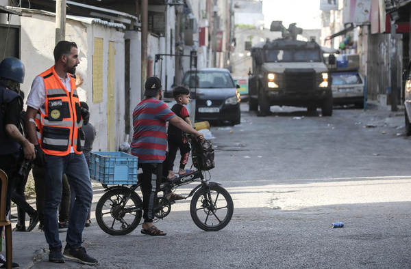 Palestinians walk past an Israeli military vehicle during a raid on the Askar refugee camp east of Nablus. Israeli forces raided and searched Palestinian homes and businesses, and fired tear gas at Palestinians.