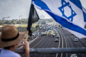 An Israeli woman holds the Israeli flag as she stands on a bridge overlooking protestors blocking the main costal Highway. Demonstrators call on Israeli Prime Minister Benjamin Netanyahu to end the war in Gaza and to release all 50 Israeli hostages held by Hamas since October 7, 2023. On what was the biggest day of national mobilization, hundreds of thousands of people poured into the streets around the country to demand a Hostage release deal and an end to the war in Gaza.