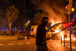 A pro-Palestinian protester is seen carrying a Palestinian flag while dumpsters burn in the background during the demonstration. A nationwide strike was held all over Spain, with demonstration in all the main cities. More than 20.000 of pro-Palestinian protesters marched in Barcelona, with several clashes with police and episodes of looting and burning of dumpsters.
