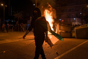 A pro-Palestinian protester is seen draped with a Palestinian flag while dumpsters burn in the background during the demonstration. A nationwide strike was held all over Spain, with demonstration in all the main cities. More than 20.000 of pro-Palestinian protesters marched in Barcelona, with several clashes with police and episodes of looting and burning of dumpsters.