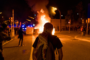 A pro-Palestinian protester is seen wearing a kufiyeh scarf while dumpsters burn in the background during the demonstration. A nationwide strike was held all over Spain, with demonstration in all the main cities. More than 20.000 of pro-Palestinian protesters marched in Barcelona, with several clashes with police and episodes of looting and burning of dumpsters.