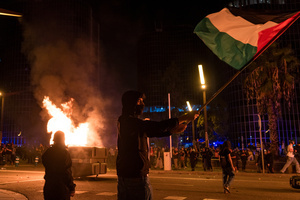 A pro-Palestinian protester is seen carrying a Palestinian flag while dumpsters burn in the background during the demonstration. A nationwide strike was held all over Spain, with demonstration in all the main cities. More than 20.000 of pro-Palestinian protesters marched in Barcelona, with several clashes with police and episodes of looting and burning of dumpsters.