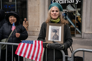 A woman, holding a photo of her father who fought as an Army Technical Sargent in the European Theater during World War II, looks towards the camera during the 106th annual Veterans Day Parade.