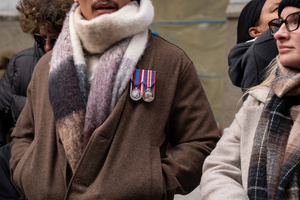 A British armed forces veteran, wearing the Queen Elizabeth II Platinum Jubilee Medal and the King Charles III Coronation Medal, views the 106th annual Veterans Day Parade from the street.