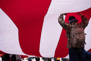 A Veteran stands underneath and holds up a large American flag during the 106th annual Veterans Day Parade.