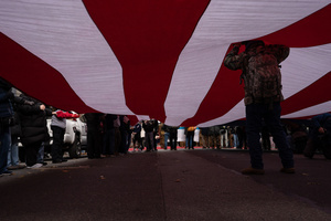 A Veteran stands underneath and holds up a large American flag during the 106th annual Veterans Day Parade.
