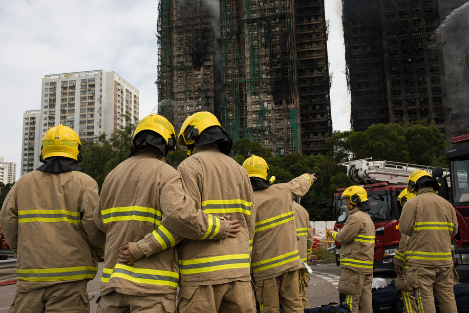 A group of firefighters is seen standing by during the operation. On Wednesday 26th November, a tower in Wang Fuk Court, which is an eight-tower complex in Tai Po, Hong Kong, caught fire while the complex had been under renovation, the towers were clad in bamboo scaffolding and mesh, it led to the rapid spread of the deadly fire to the other six towers. The incident soon escalated to Level 5 fire, for the first time in 17 years. After an overnight rescue operation by firefighters and police force, the fire was reportedly under control. The death toll has been rising following the continuation of the rescue work. Many local residents have also volunteered to allocate and deliver emergency supplies to displaced residents of the complex.