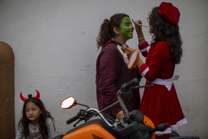 A woman is made up like the Grinch, and next to her sits a little girl with devil horns, during the Burning of the Devil on the eve of the celebration of the Virgin of the Immaculate Conception, festivities that mark the beginning of Christmas in Guatemala.