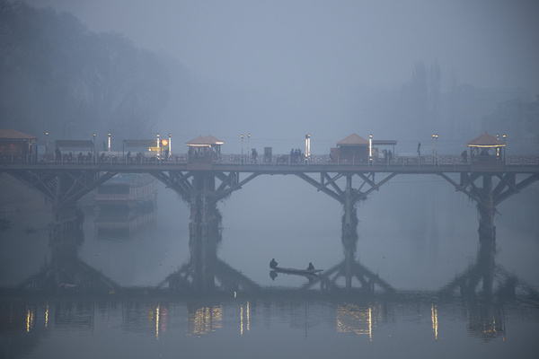 A fisherman rows his boat as people walk on a footbridge over the Jhelum River on a cold and foggy evening in Srinagar. Kashmir is in the grip of an intense cold wave, with dense fog persisting across several parts of the Valley. Data from Air Quality India show that multiple areas in Jammu and Kashmir have recorded an Air Quality Index above 288, placing them in the “Very Poor” category under international standards.