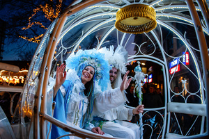 Two actors inside the carriage are smiling at the camera. The Winter Wonder Parade marks the festive opening of the annual Nijmegen Winter Weeks. This enchanting spectacle features a fairytale procession including a winter carriage pulled by white horses, ice queens on stilts, musicians, dancers, and jugglers. The parade departs from the Lindenberg at 4:30 PM and concludes at the Grote Markt, where the Christmas tree lighting officially starts three weeks of winter magic.