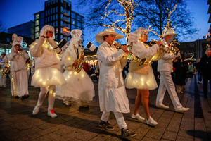 A music band wearing small lights is performing during the parade. The Winter Wonder Parade marks the festive opening of the annual Nijmegen Winter Weeks. This enchanting spectacle features a fairytale procession including a winter carriage pulled by white horses, ice queens on stilts, musicians, dancers, and jugglers. The parade departs from the Lindenberg at 4:30 PM and concludes at the Grote Markt, where the Christmas tree lighting officially starts three weeks of winter magic.