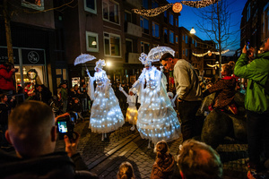 People are seen taking photos of the acrobats on the crowded streets. The Winter Wonder Parade marks the festive opening of the annual Nijmegen Winter Weeks. This enchanting spectacle features a fairytale procession including a winter carriage pulled by white horses, ice queens on stilts, musicians, dancers, and jugglers. The parade departs from the Lindenberg at 4:30 PM and concludes at the Grote Markt, where the Christmas tree lighting officially starts three weeks of winter magic.