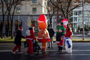 A group of people take photos with a couple of people in inflatable costumes during a charity race. A charity race was organized by the Spanish department store chain El Corte Ingles where participants, mostly families, run dressed as Santa Claus or in Christmas-themed costumes.
