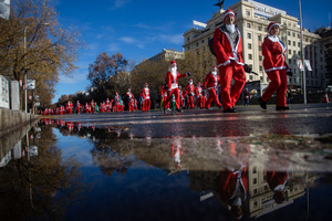 Several people participating in a charity race are reflected in a puddle. A charity race was organized by the Spanish department store chain El Corte Ingles where participants, mostly families, run dressed as Santa Claus or in Christmas-themed costumes.