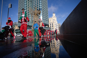 Several people participating in a charity race are reflected in a puddle. A charity race was organized by the Spanish department store chain El Corte Ingles where participants, mostly families, run dressed as Santa Claus or in Christmas-themed costumes.