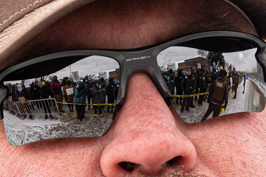 Protesters demonstrating against Immigration and Customs Enforcement (ICE) are reflected in a Sheriff's deputy's sunglasses in Minneapolis.