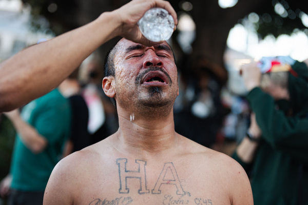 A man struggles to recover after being tear-gassed as another protester pours water over his head outside the Metropolitan Detention Center in Los Angeles during the National Day of Action against ICE.