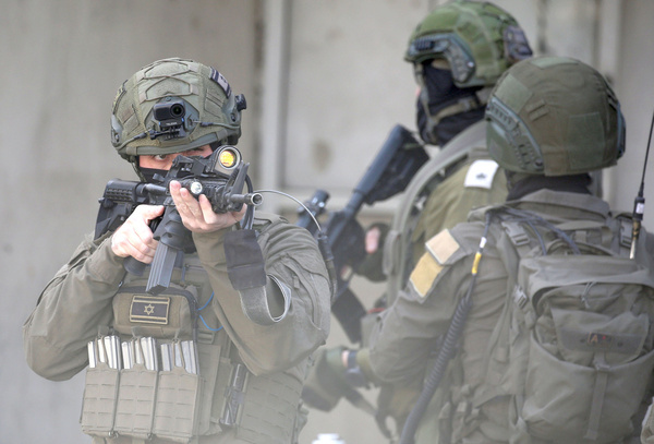 An Israeli soldier points his weapon at Palestinians to prevent them from entering a market during a security operation in Balata refugee camp, east of Nablus. Israeli forces entered the market and closed the camp's entrance. Soldiers also raided shops, arrested residents, and interrogated them about the security situation in Balata camp.