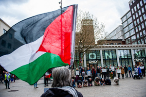 A woman holding a Palestinian flag is seen watching the performance. Activists performed as the Palestinian hostages held by the Israel government during a silent procession through the city to demand their release and against Israel's new execution law. With this protest, Nijmegen for Palestine wants to draw attention to the Palestinian hostages, who are often held for months, even years, without charge in appalling Israeli detention camps.