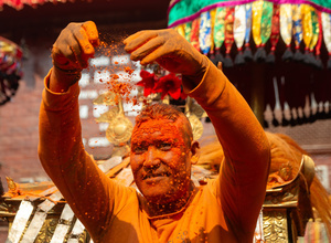 The reveler smears the vermilion powder at his face during the Festival. Sindoor Jatra or vermillion powder festival is celebrated each year to welcome the start of spring and Nepalese New Year, by playing a traditional instrument, singing, dancing, and carrying chariots of several gods and goddesses around the place.