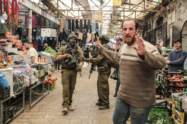 A Palestinian walks past Israeli soldiers in the center of the Old City market in Nablus during a security operation. Israeli forces raided the market, targeting shops. Dozens of Palestinians were arrested in West Bank cities under the control of the Palestinian Authority, headed by President Mahmoud Abbas.
