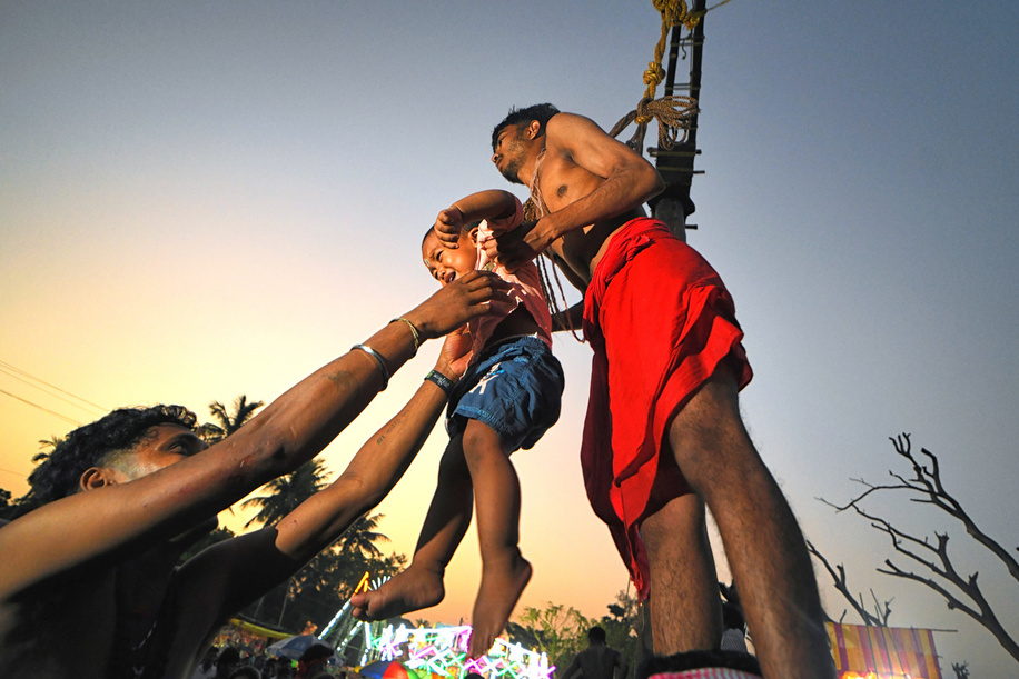 A Hindu devotee hangs on a hook while carrying a little baby during Charak Puja Celebration. The Charak Festival is one of the oldest Folk festivals where devotees show their faith by self inflicting pain on themselves, in the belief that Lord Shiva will help them overcome troubles in their daily lives.