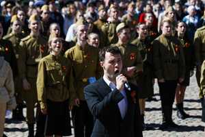 A male soloist performs a song on stage in front of participants in historical and modern military uniforms during the "Victory Ball" event. A large-scale theatrical reconstruction and flash mob titled "Victory Ball" (Bal Pobedy) takes place on the Cathedral Square of the Peter and Paul Fortress. The event is dedicated to the 81st anniversary of the victory in World War II (WWII). Hundreds of participants, including youth activists, members of the Yunarmia movement, and students in historical and modern military uniforms, perform mass dances and formations. The reconstruction is part of the city-wide celebrations ahead of Victory Day in St. Petersburg.