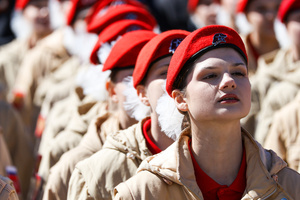 A close-up of a young woman member of the Yunarmia youth movement in a red beret singing with emotion during a mass flash mob dedicated to the 81st anniversary of Victory Day. A large-scale theatrical reconstruction and flash mob titled "Victory Ball" (Bal Pobedy) takes place on the Cathedral Square of the Peter and Paul Fortress. The event is dedicated to the 81st anniversary of the victory in World War II (WWII). Hundreds of participants, including youth activists, members of the Yunarmia movement, and students in historical and modern military uniforms, perform mass dances and formations. The reconstruction is part of the city-wide celebrations ahead of Victory Day in St. Petersburg.