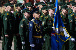 Military personnel and cadets in dark green uniforms stand with a blue ceremonial flag during the "Victory Ball" theatrical reconstruction on Cathedral Square. A large-scale theatrical reconstruction and flash mob titled "Victory Ball" (Bal Pobedy) takes place on the Cathedral Square of the Peter and Paul Fortress. The event is dedicated to the 81st anniversary of the victory in World War II (WWII). Hundreds of participants, including youth activists, members of the Yunarmia movement, and students in historical and modern military uniforms, perform mass dances and formations. The reconstruction is part of the city-wide celebrations ahead of Victory Day in St. Petersburg.